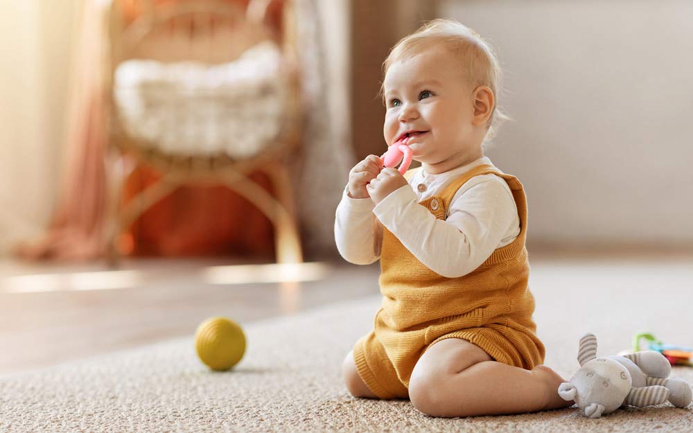 Le bébé est assis à genoux sur le sol et joue avec un anneau de dentition rose.