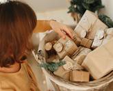 Christmas Advent calendar for kids. Girl wearing mustard linen dress looking at basket with advent gifts boxes on wooden cabinet. Eco friendly christmas