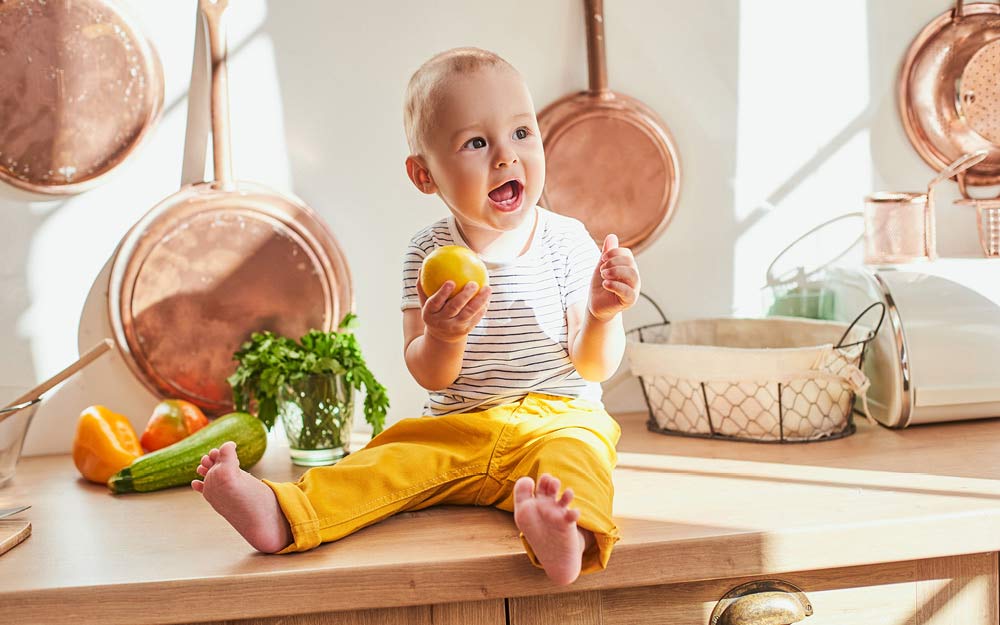 Bébé est assis en riant sur le plan de travail de la cuisine, une citron à la main.