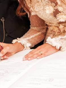 Les mariés signent les documents officiels de leur mariage à une table, la mariée tenant un stylo.