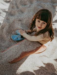 Une fillette d’environ 8 ans, assise sur la plage, les jambes pleines de sable et le regard tourné vers l’horizon
