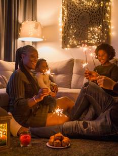 Une famille réunie dans un salon décoré pour Noël partage un moment chaleureux avec des cierges magiques près du sapin illuminé.