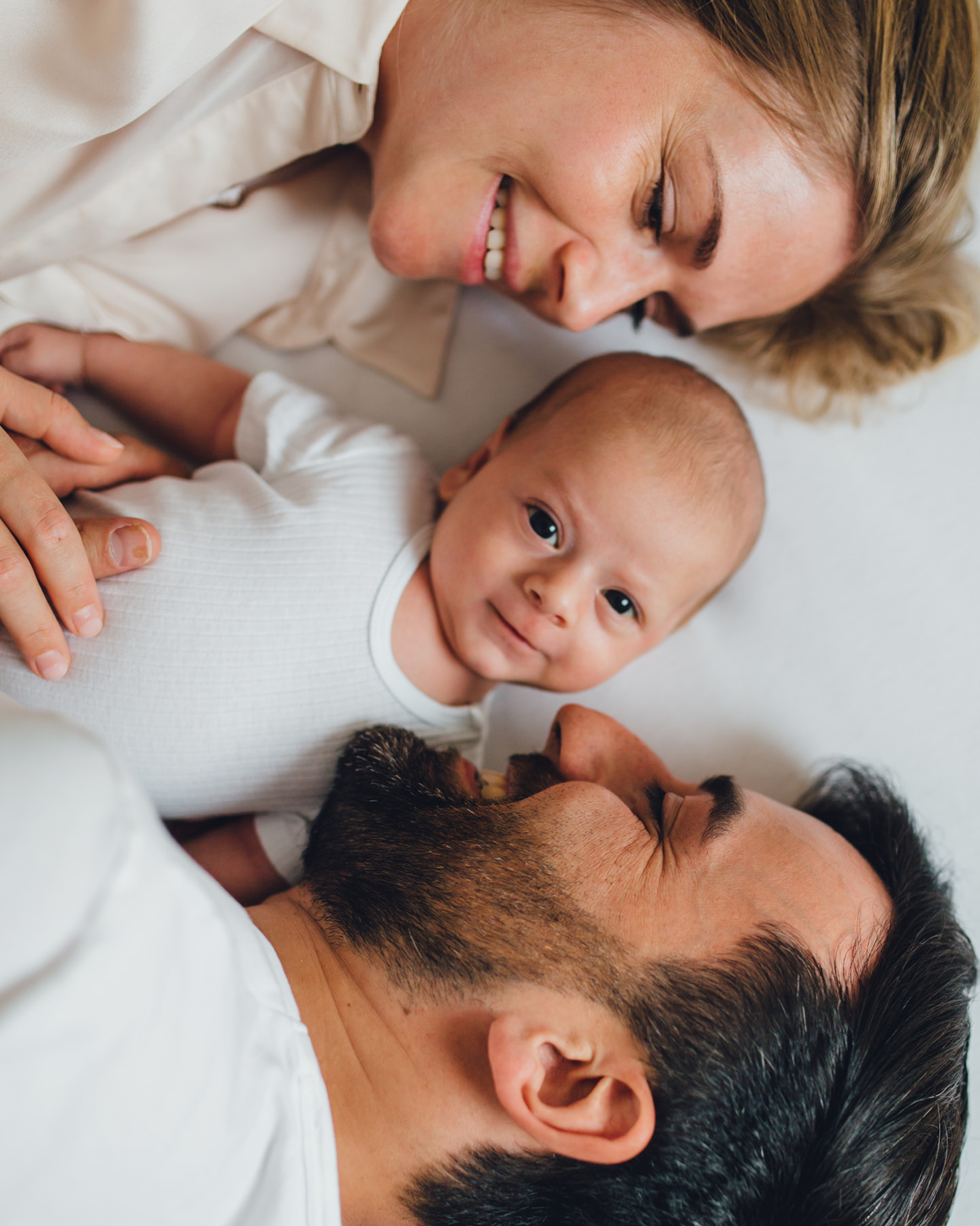 Des parents au lit, avec leur bébé souriant au centre