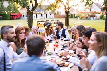 Wedding reception outside in the backyard. Bride and groom with family and guests sitting around the table, having fun.