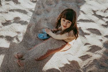 Une fillette d’environ 8 ans, assise sur la plage, les jambes pleines de sable et le regard tourné vers l’horizon