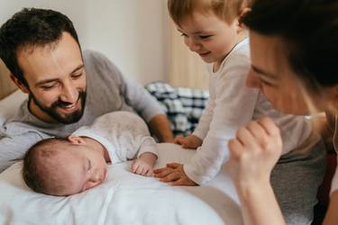Des parents allongés avec leur bébé endormi et leur aîné tout sourire dans le lit.
