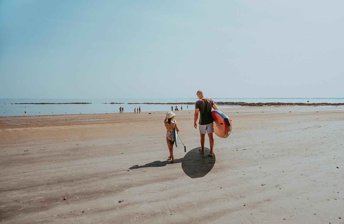 Un père et sa fille d’environ 8 ans marchent ensemble vers l’eau sur la plage.