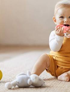 Le bébé est assis sur le tapis et joue avec un anneau de dentition rose.