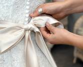 Gros plan sur des mains féminines nouant délicatement un ruban de satin sur une robe de mariée.