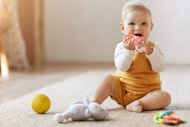 Le bébé est assis sur le tapis et joue avec un anneau de dentition rose.