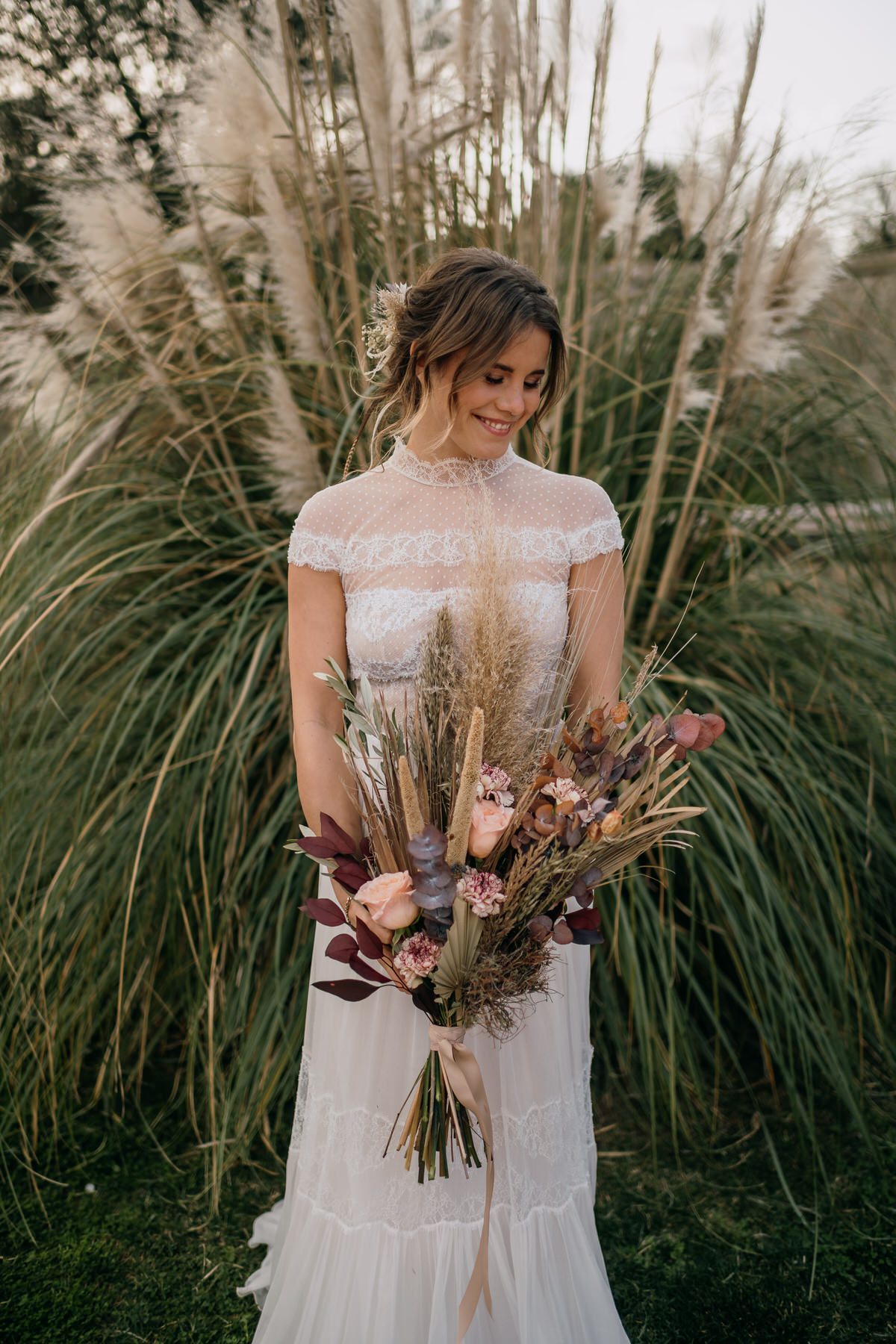 Une mariée devant des herbes de Pampas avec un bouquet de fleurs séchées champêtre