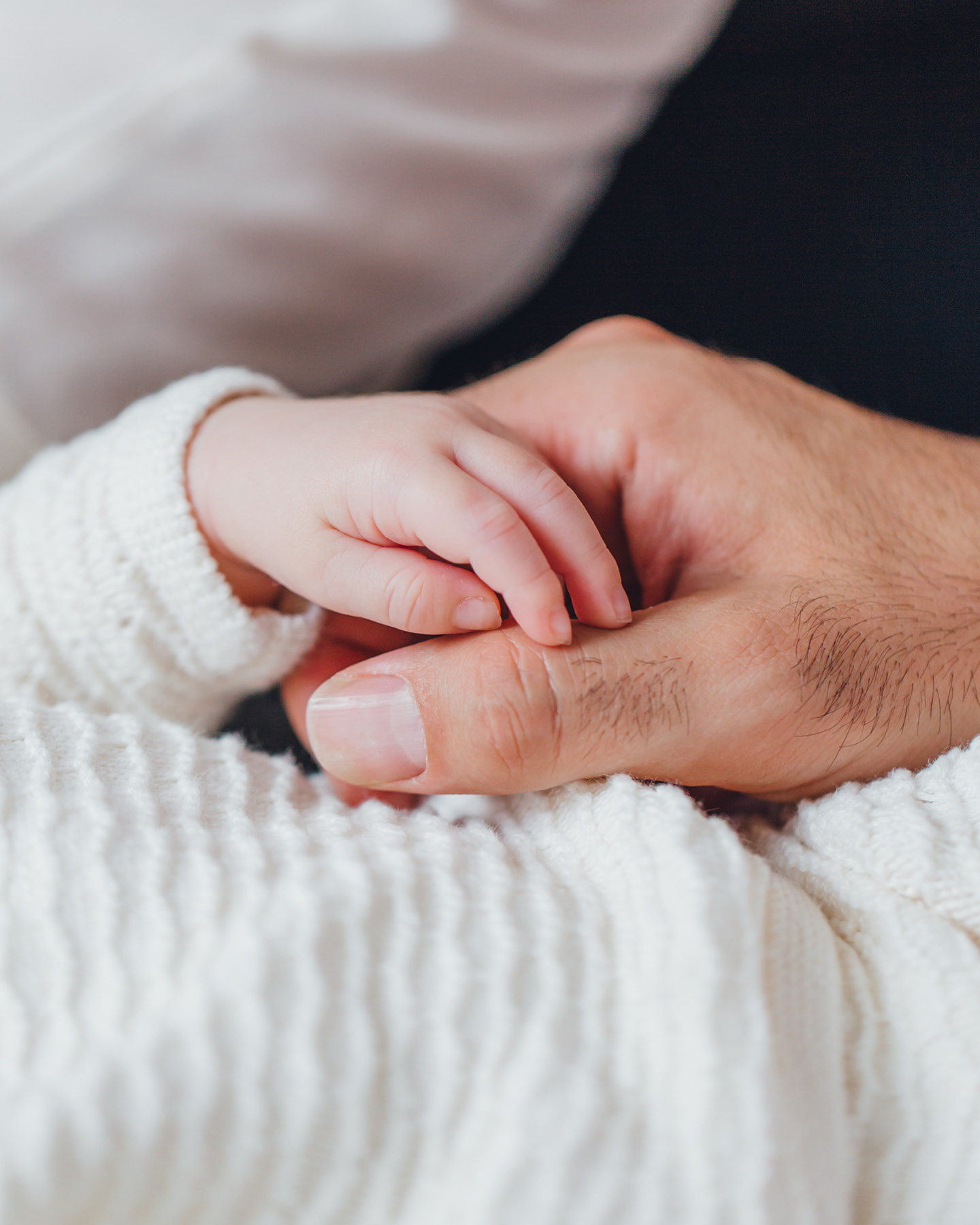 Gros plan : un papa tient la minuscule main de son bébé