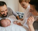 Des parents allongés avec leur bébé endormi et leur aîné tout sourire dans le lit.