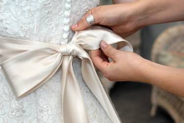 Gros plan sur des mains féminines nouant délicatement un ruban de satin sur une robe de mariée.