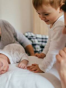 Des parents allongés avec leur bébé endormi et leur aîné tout sourire dans le lit.