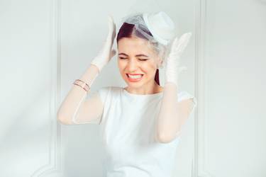 Beautiful young woman in elegant bridal outfit holding hands near temples in stress while frowning on white background