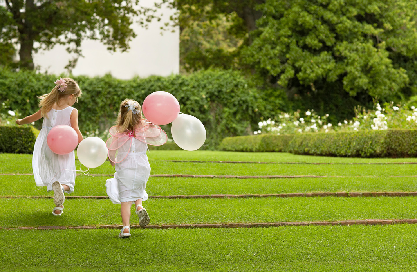 Deux petites filles vêtues de blanc jouent avec des ballons dans un parc lors d’un mariage.