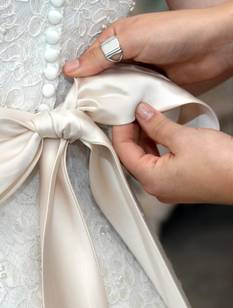 Gros plan sur des mains féminines nouant délicatement un ruban de satin sur une robe de mariée.