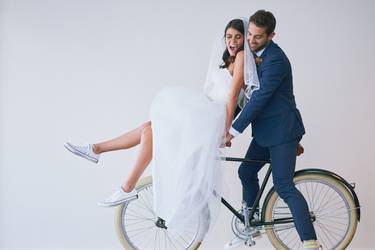 Studio shot of a newly married young couple riding a bicycle together against a gray background