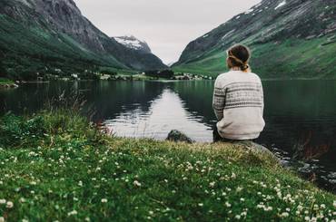 Young caucasian woman sitting near the mountain lake in Norway
