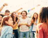 Un groupe d’amis fête un anniversaire en plein air ; un homme souriant tient un gâteau orné du chiffre 30, entouré de décorations colorées et de convives joyeux.