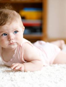 Bébé, allongé sur le ventre sur le tapis, essaie de ramper.